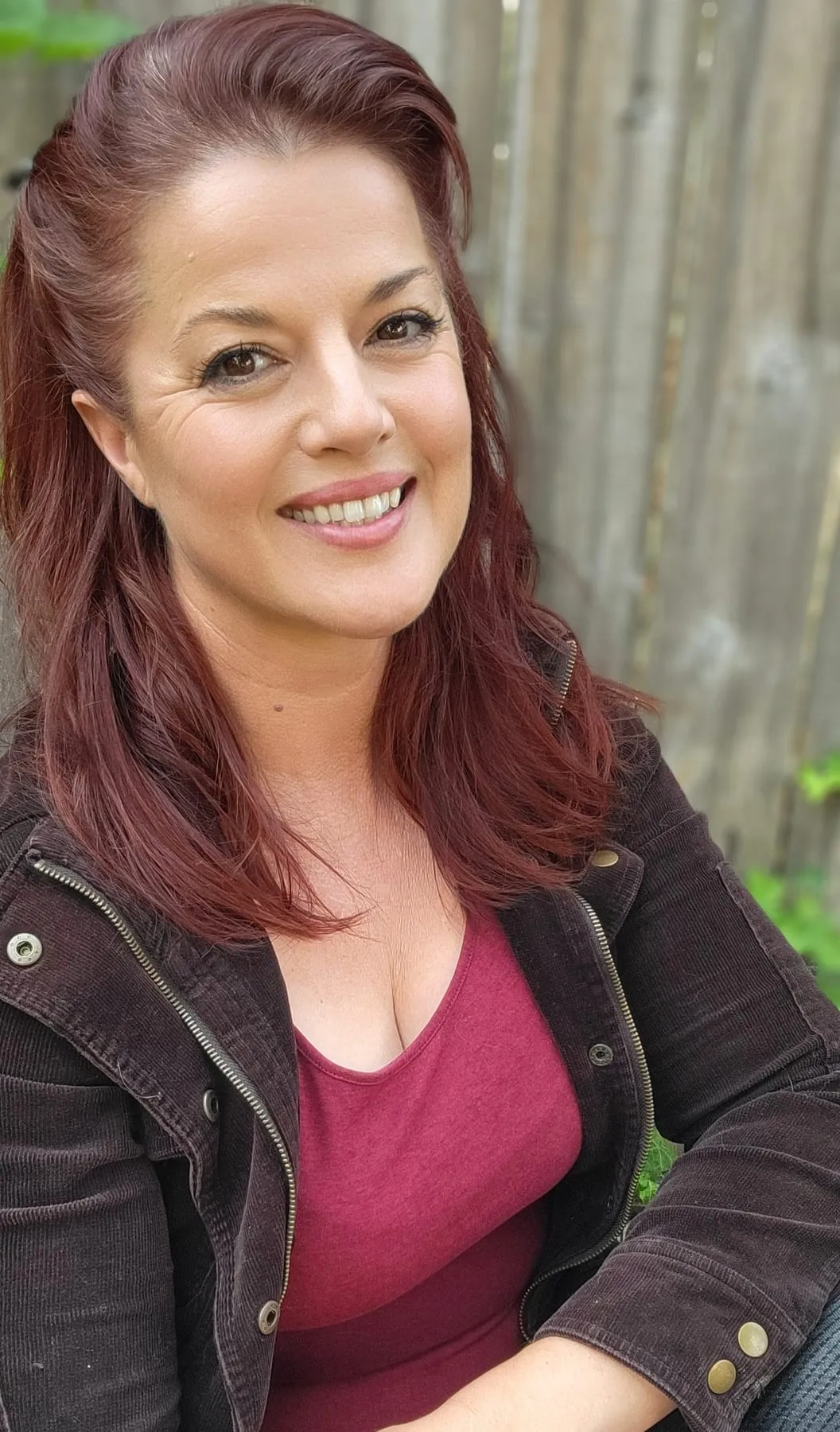 Mackenzie, who writes and edits the videos, smiling outdoors by a wood fence.